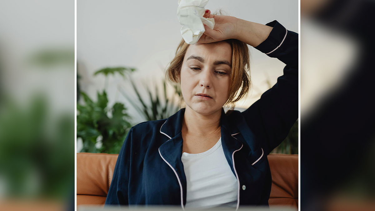Tired woman in pajamas holding tissue to forehead, reflecting stress from family trip and boyfriend family conflict.