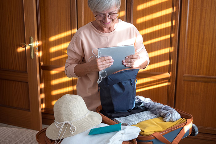 Older woman packing a suitcase for vacation, holding a tablet, showing mom booked a vacation and won't babysit kids. Older woman packing a suitcase for vacation, holding a tablet, showing mom booked a vacation and won't babysit kids.