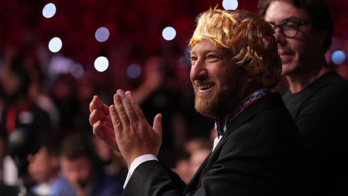 Man with a blond wig and beard clapping in a crowded dimly lit venue, relating to Dave Portnoy net worth topics.