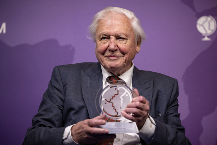 David Attenborough in a suit holding an award, discussing his diet of fish and cheese instead of red meat. David Attenborough in a suit holding an award, discussing his diet of fish and cheese instead of red meat.