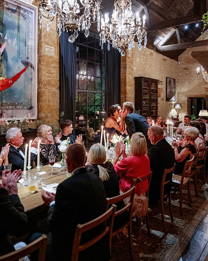 Guests seated at a long dining table with candles during David Beckham's 50th birthday party amid family tension. Guests seated at a long dining table with candles during David Beckham's 50th birthday party amid family tension.