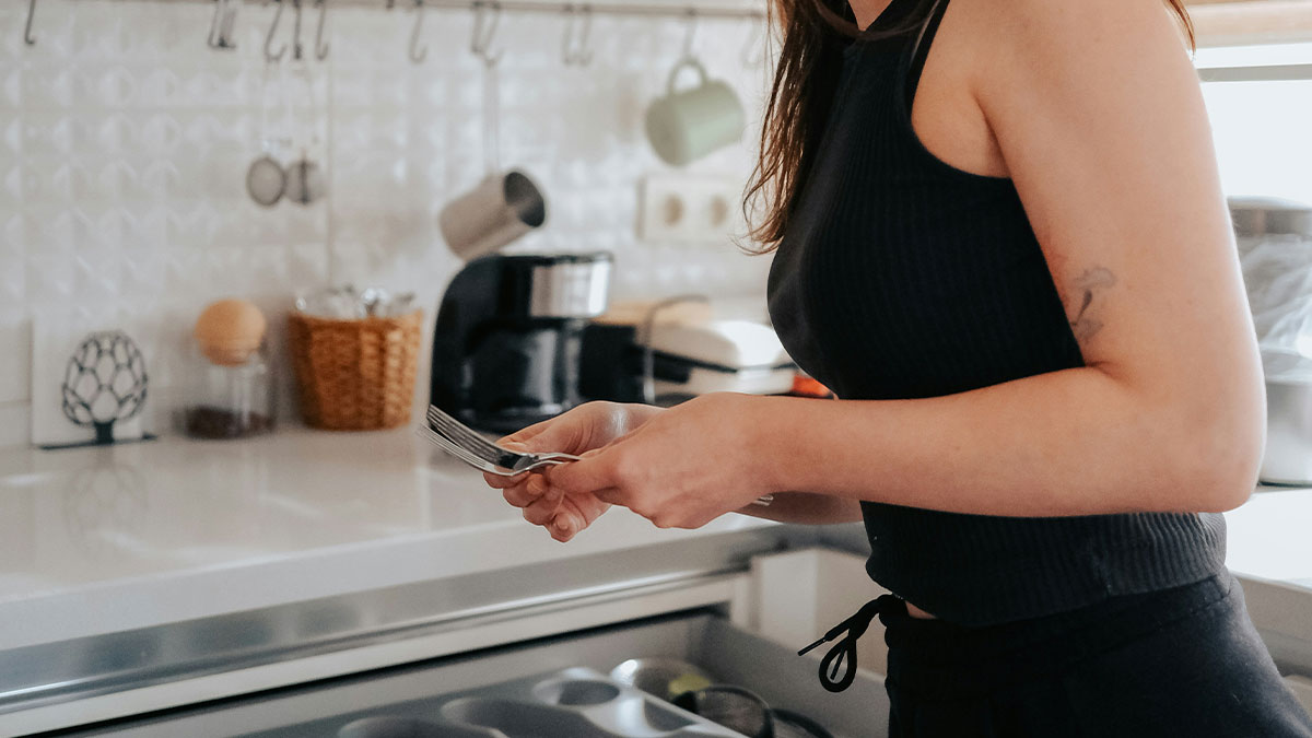 Woman holding kitchen utensils by an open drawer in a modern kitchen after couple rents home to friends.