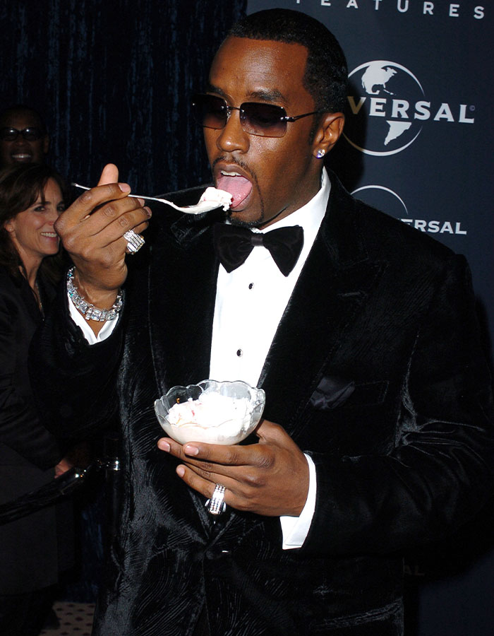 Diddy wearing sunglasses and a black tuxedo, eating dessert from a glass bowl at a formal event. Diddy wearing sunglasses and a black tuxedo, eating dessert from a glass bowl at a formal event.