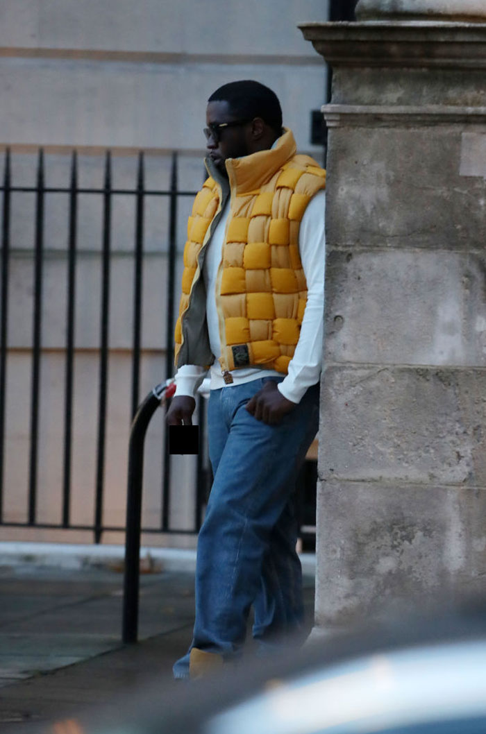 Diddy wearing a yellow puffer vest and sunglasses standing by a stone wall, illustrating Diddy’s net worth legal trouble impact.
