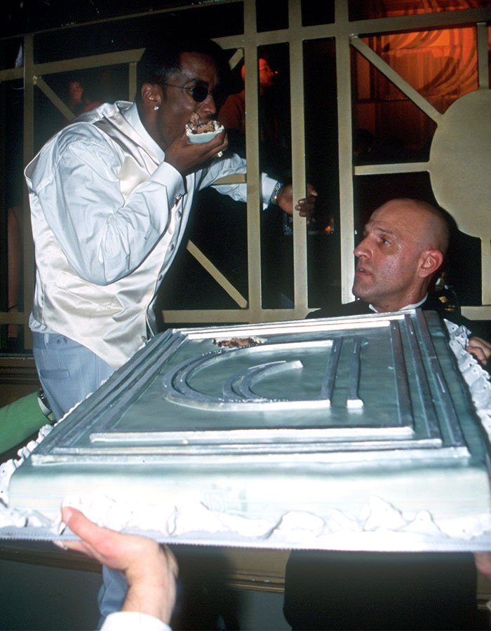 Man eating cake messily while another person holds the large cake, highlighting Diddy’s revolting eating habits revealed by staff. Man eating cake messily while another person holds the large cake, highlighting Diddy’s revolting eating habits revealed by staff.