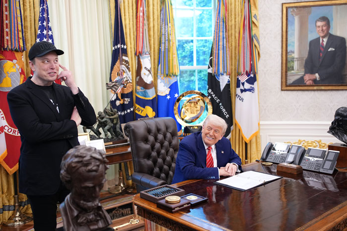 Elon Musk standing with a black eye and head ticks alongside a man seated at the Oval Office desk. Elon Musk standing with a black eye and head ticks alongside a man seated at the Oval Office desk.
