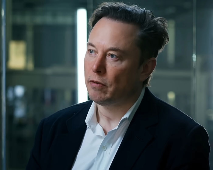 Elon Musk in a formal suit, speaking in an indoor corporate setting, related to Tesla CEO search news. Elon Musk in a formal suit, speaking in an indoor corporate setting, related to Tesla CEO search news.
