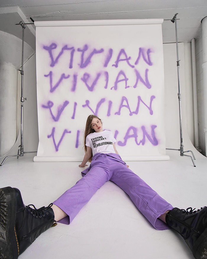 Vivian Musk posing for modeling debut against a backdrop with her name in purple graffiti-style letters. Vivian Musk posing for modeling debut against a backdrop with her name in purple graffiti-style letters.