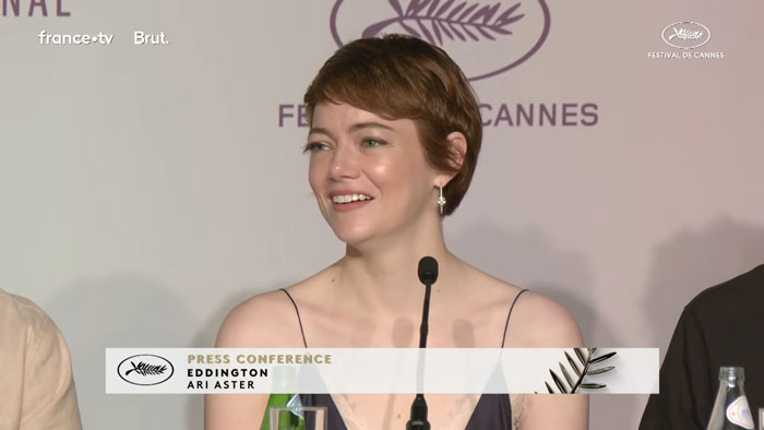 Emma Stone responds to reporter during Cannes press conference, smiling and speaking at microphone. Emma Stone responds to reporter during Cannes press conference, smiling and speaking at microphone.