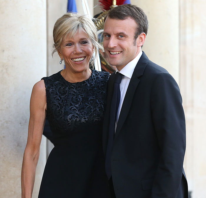 French President Emmanuel Macron with his wife smiling, related to lip reader revealing words after shoving incident. French President Emmanuel Macron with his wife smiling, related to lip reader revealing words after shoving incident.