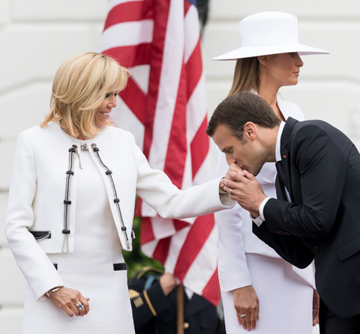 French President Emmanuel Macron kissing a woman's hand during a formal event with American flag in the background French President Emmanuel Macron kissing a woman's hand during a formal event with American flag in the background