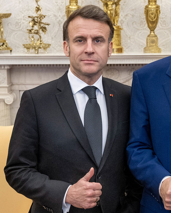 French President Emmanuel Macron giving thumbs up with a suit and tie amid Lip Reader analysis after shoving incident.