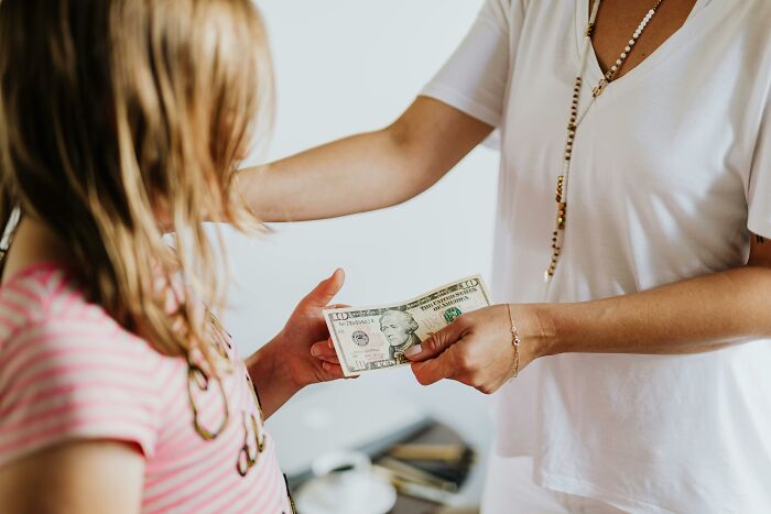 Child receiving money from an adult, highlighting jealous grandparents wanting ex-in-laws to stop giving kid money. Child receiving money from an adult, highlighting jealous grandparents wanting ex-in-laws to stop giving kid money.