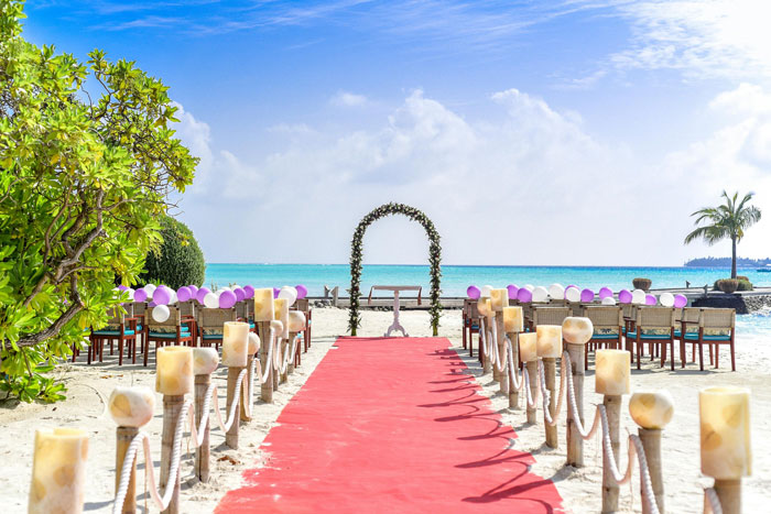 Beach wedding venue decorated with chairs, an arch, and a red carpet aisle under a clear blue sky. Beach wedding venue decorated with chairs, an arch, and a red carpet aisle under a clear blue sky.