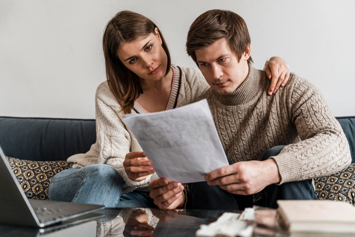 Couple planning wedding venue three years ahead, looking concerned while reviewing documents together at home. Couple planning wedding venue three years ahead, looking concerned while reviewing documents together at home.