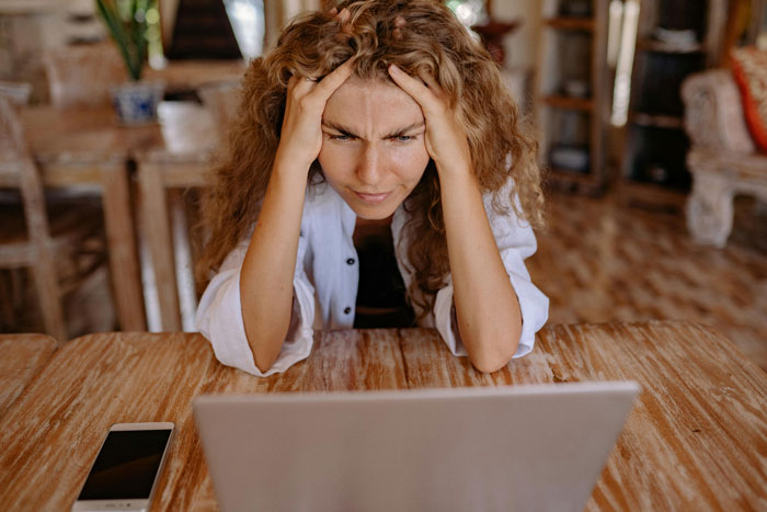 Woman looking stressed while using laptop at wooden table, relating to couple booking wedding venue years in advance dilemma. Woman looking stressed while using laptop at wooden table, relating to couple booking wedding venue years in advance dilemma.
