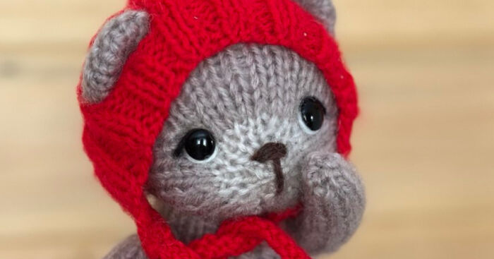 Knitted gray animal with black eyes wearing a red hat, showcasing an easy and quick to make knitting pattern project.