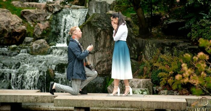 Man kneeling proposing marriage to woman by a waterfall in the Kyoto Garden, capturing a secret marriage proposal moment.
