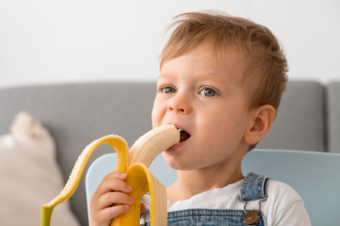 Toddler enjoying a peeled banana, showing a son's veggie love with healthy fruit over traditional meals. Toddler enjoying a peeled banana, showing a son's veggie love with healthy fruit over traditional meals.