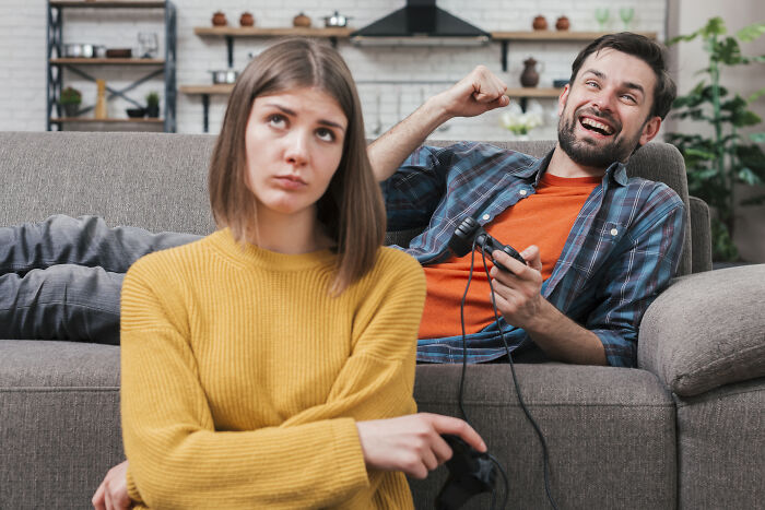 A man happily playing video games while his upset girlfriend turns away showing relationship tension after girlfriend's demand.