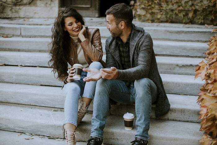 A young couple sitting on outdoor steps drinking coffee, illustrating guys who turned their back on female friends.