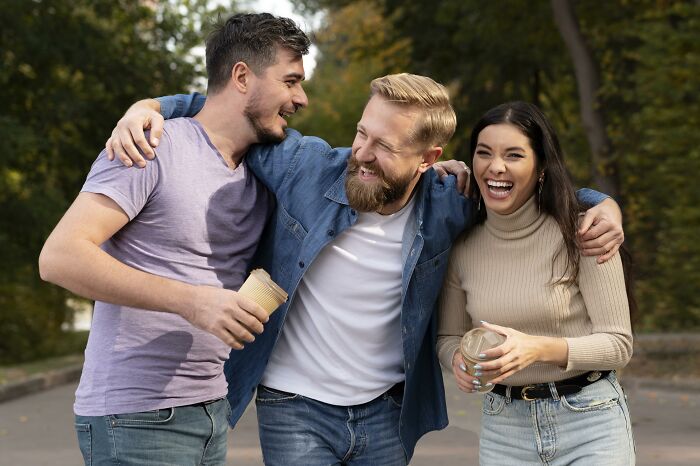 Three friends laughing outdoors, showing close male friendships and social bonds among guys and female friends.