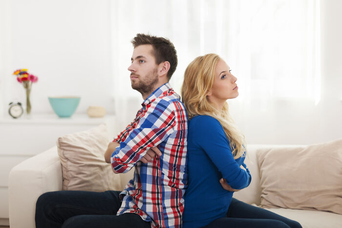 Young couple sitting back to back on a couch, illustrating the impact of turning back on female friends after a girlfriend’s demand.