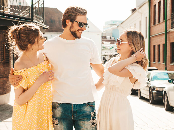 Man with sunglasses smiling between two female friends outdoors, representing guys who turned their back on female friends.