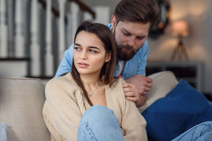 A man comforting his upset girlfriend on a couch, reflecting relationship struggles with female friends involved.