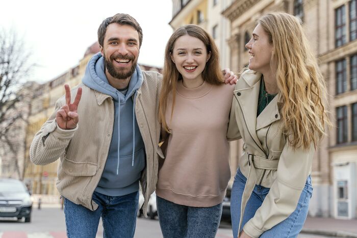 Three friends smiling outdoors, capturing moments of friendship and connection among men and women in casual attire.