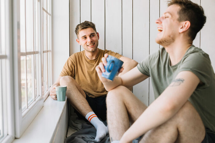 Two young men enjoying coffee and laughing together, reflecting friendships tested by relationship demands.