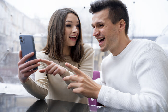 A man and woman smiling and looking at a smartphone, illustrating lost friendships and ultimatums between friends.