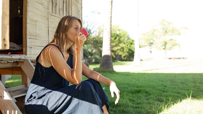 Woman sitting outside on wooden steps drinking from a red cup, related to neighbor’s pink flamingos Facebook campaign.