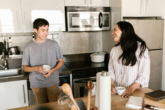 Young couple in kitchen holding mugs, discussing plans for a steamy weekend amid roomie eviction tension. Young couple in kitchen holding mugs, discussing plans for a steamy weekend amid roomie eviction tension.