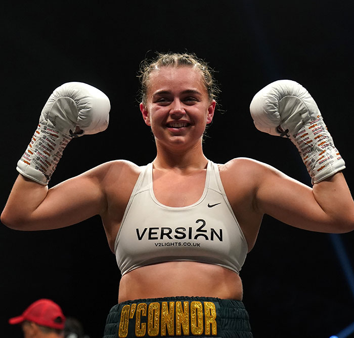 Pro boxer Georgia O’Connor smiling and raising her gloves in victory during a professional boxing match. Pro boxer Georgia O’Connor smiling and raising her gloves in victory during a professional boxing match.