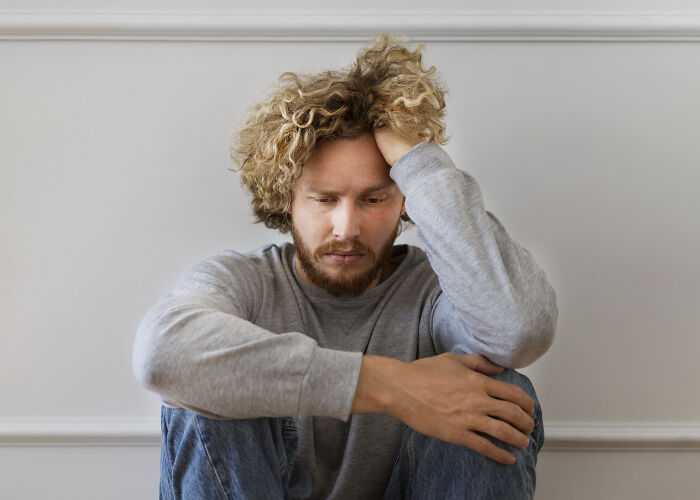 Young man with curly hair sitting on the floor, looking distressed, representing men who lost amazing partners.