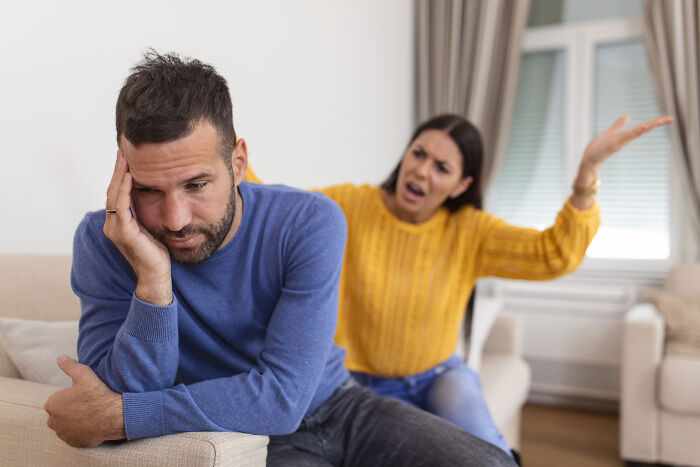 Man looking distressed sitting on couch while woman behind him gestures angrily, illustrating men who lost amazing partners.
