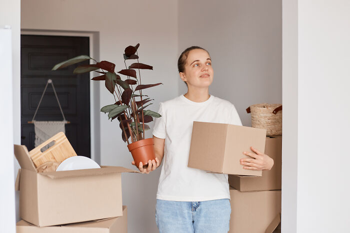 Young man holding a plant and a box among moving boxes, reflecting on life after losing amazing partners.
