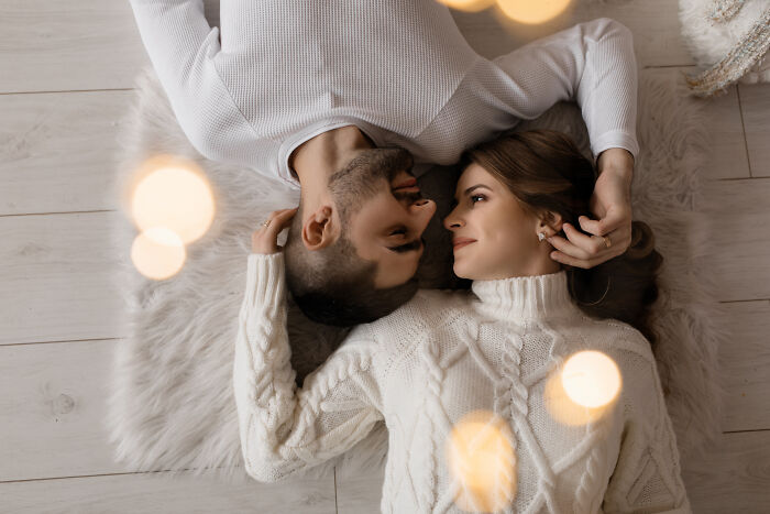 Couple lying on a soft rug, wearing cozy sweaters, sharing an intimate moment reflecting on love and loss.