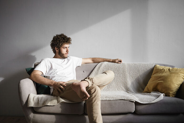 Young man sitting alone on a couch looking pensive, reflecting on life after losing an amazing partner.