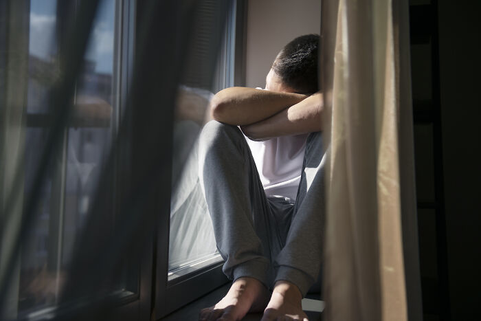 Man sitting alone by a window, head resting on arms, reflecting on life after losing an amazing partner.