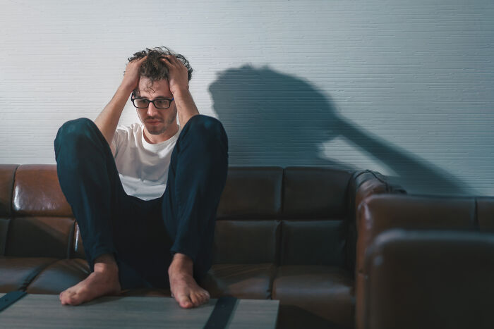 Man sitting barefoot on couch, holding head in hands, reflecting on life after losing amazing partner.