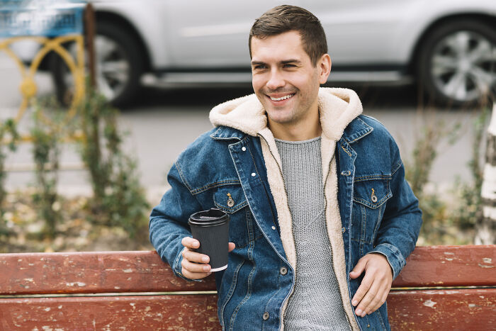 Young man holding coffee cup on park bench, reflecting on life after losing amazing partner, sharing his experience.