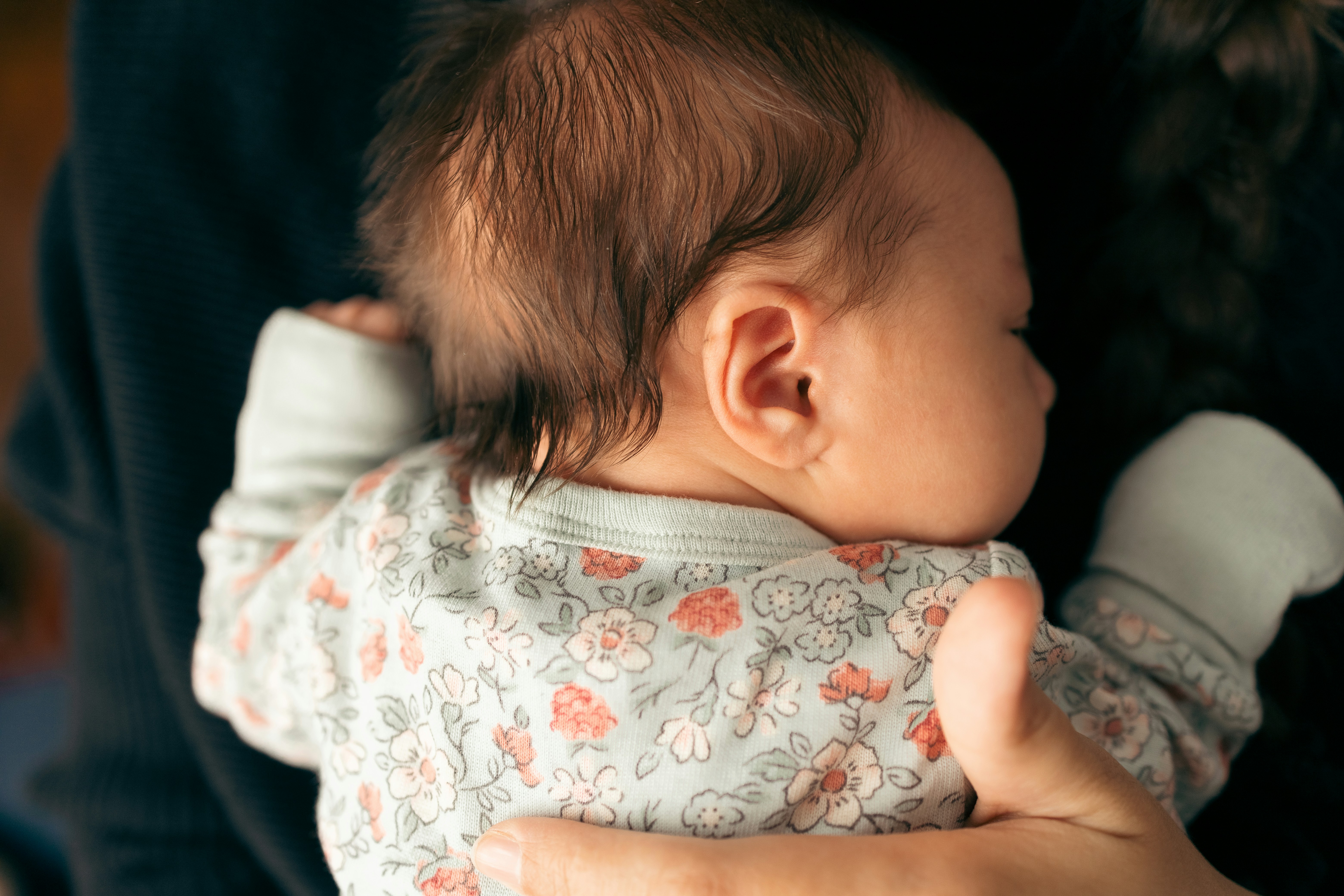 Close-up of a baby in floral clothes being gently held, relating to keeping son away from grandmother after fed custard. Close-up of a baby in floral clothes being gently held, relating to keeping son away from grandmother after fed custard.