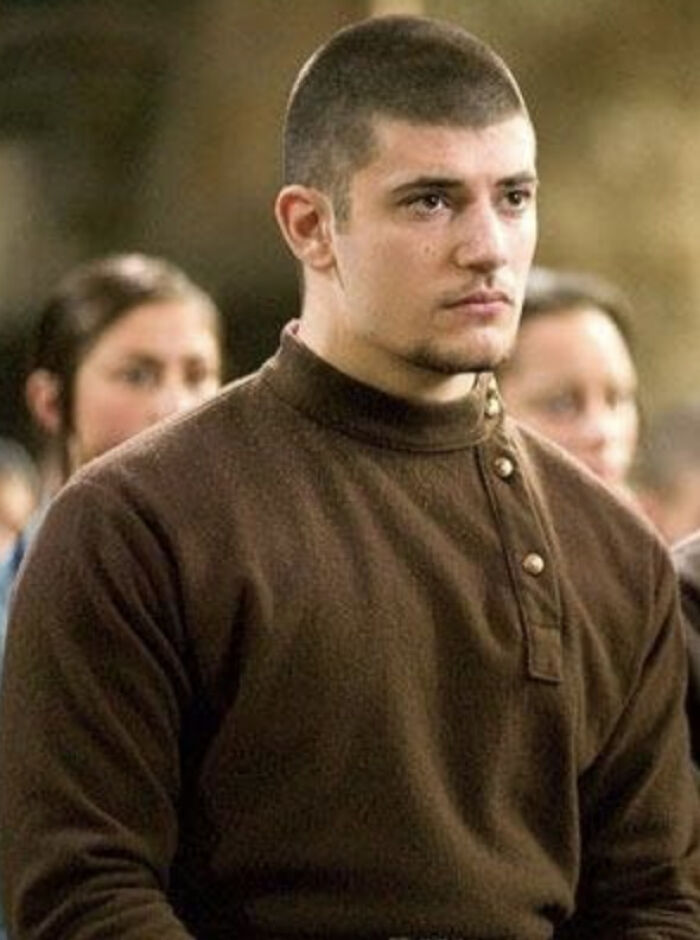 Actor who played Viktor Krum in Harry Potter looking serious in a brown sweater during a film scene with blurred people in background Actor who played Viktor Krum in Harry Potter looking serious in a brown sweater during a film scene with blurred people in background