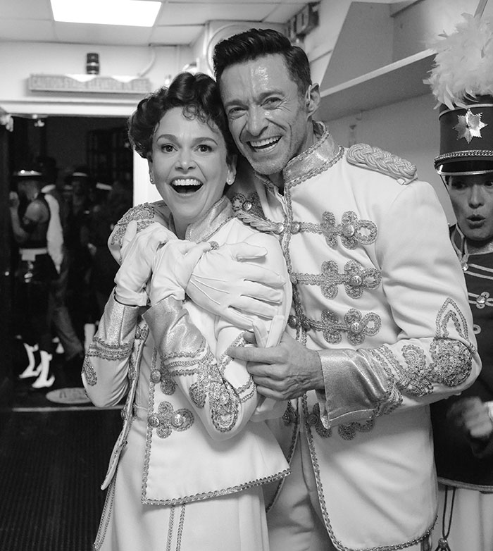 Hugh Jackman and Sutton Foster smiling backstage in matching ornate costumes during a theatrical performance. Hugh Jackman and Sutton Foster smiling backstage in matching ornate costumes during a theatrical performance.
