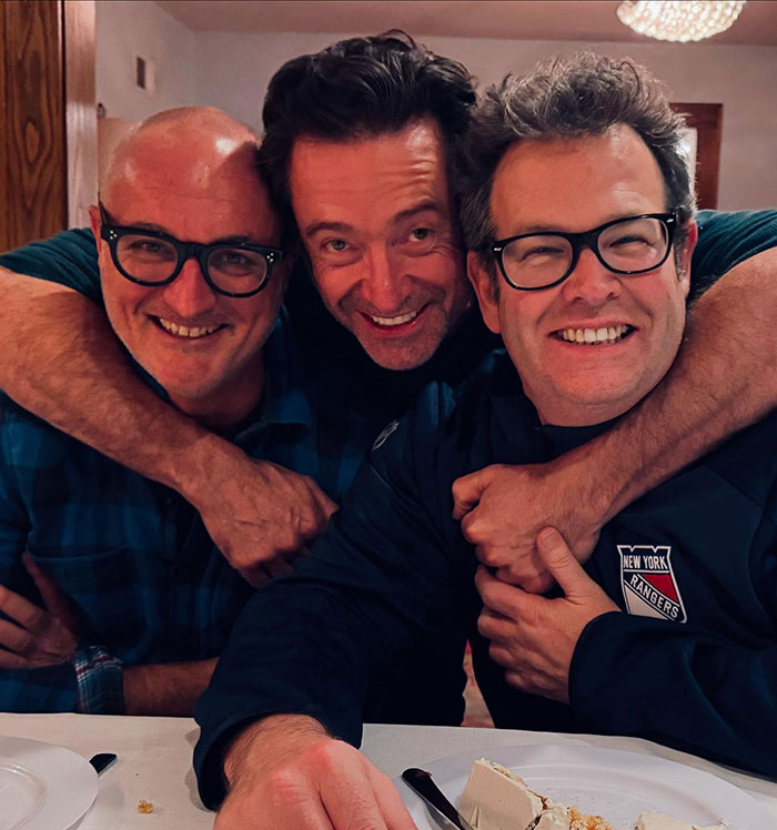 Hugh Jackman with childhood friends, smiling and embracing during a casual indoor gathering. Hugh Jackman with childhood friends, smiling and embracing during a casual indoor gathering.