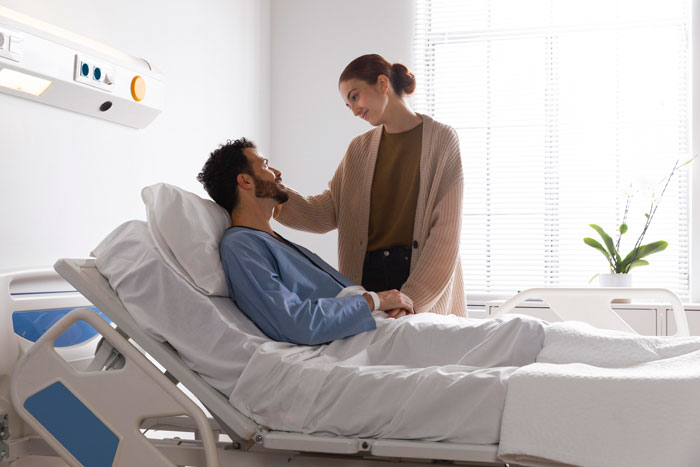 Man in hospital bed with woman comforting him, illustrating a sensitive moment related to telling kids about their dad's passing. Man in hospital bed with woman comforting him, illustrating a sensitive moment related to telling kids about their dad's passing.