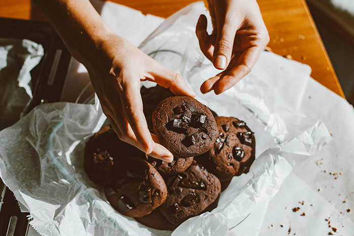 Hands holding a chocolate cookie from a box of sweets, representing a flirty dad dropping off treats at school. Hands holding a chocolate cookie from a box of sweets, representing a flirty dad dropping off treats at school.