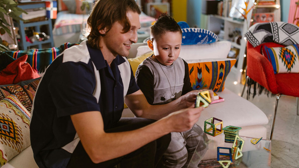 Dad and son playing with colorful magnetic building toys at home, hinting at flirty dad dropping off sweets at school.